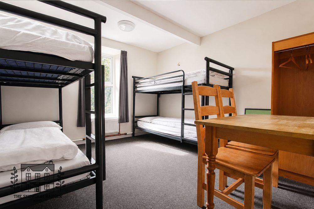 Shared dorm room with two bunk beds, a wooden table, and chairs on carpeted floor