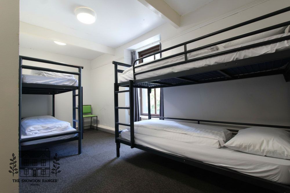 Dorm room with three black bunk beds, white bedding, and a green chair under bright ceiling lights