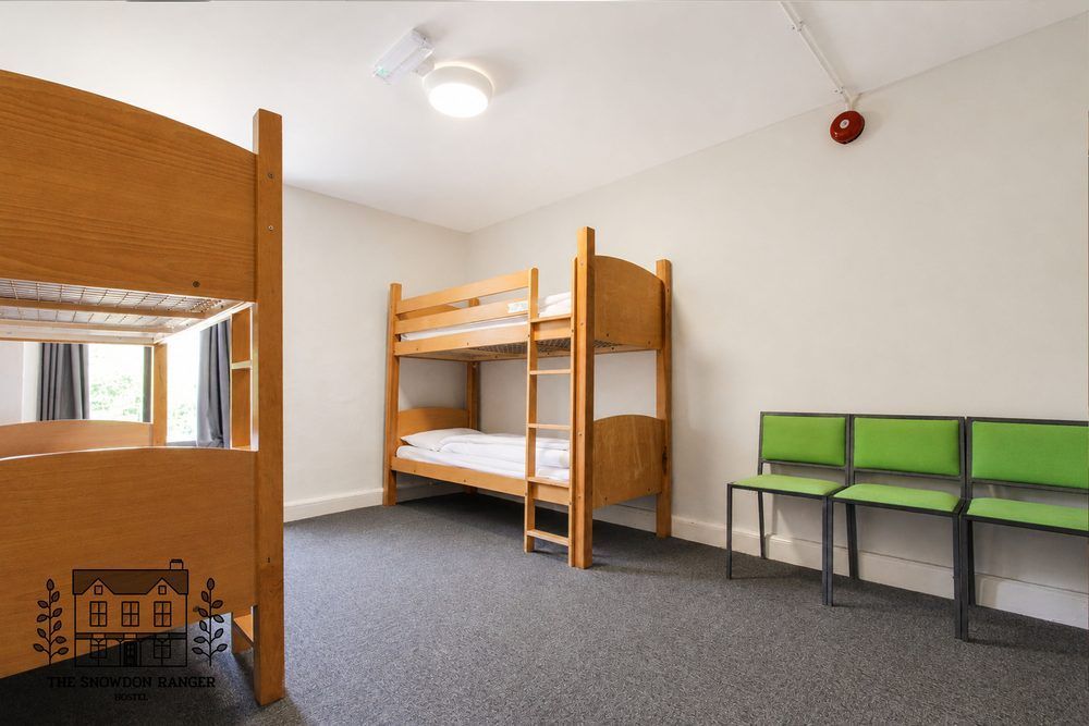 Small dorm room with a wooden bunk bed, green bench seating, and a round mirror.