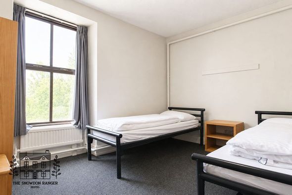 Small bedroom with two single beds, a window, and a nightstand in a simple white-walled room