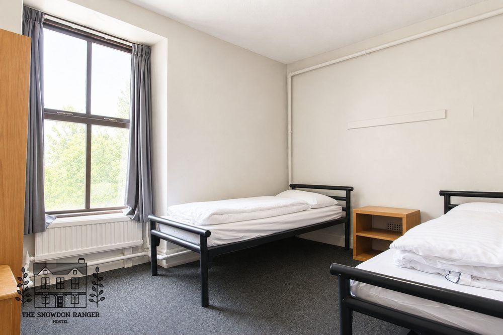 Sparse bedroom with two single beds, a window, and a small wooden nightstand