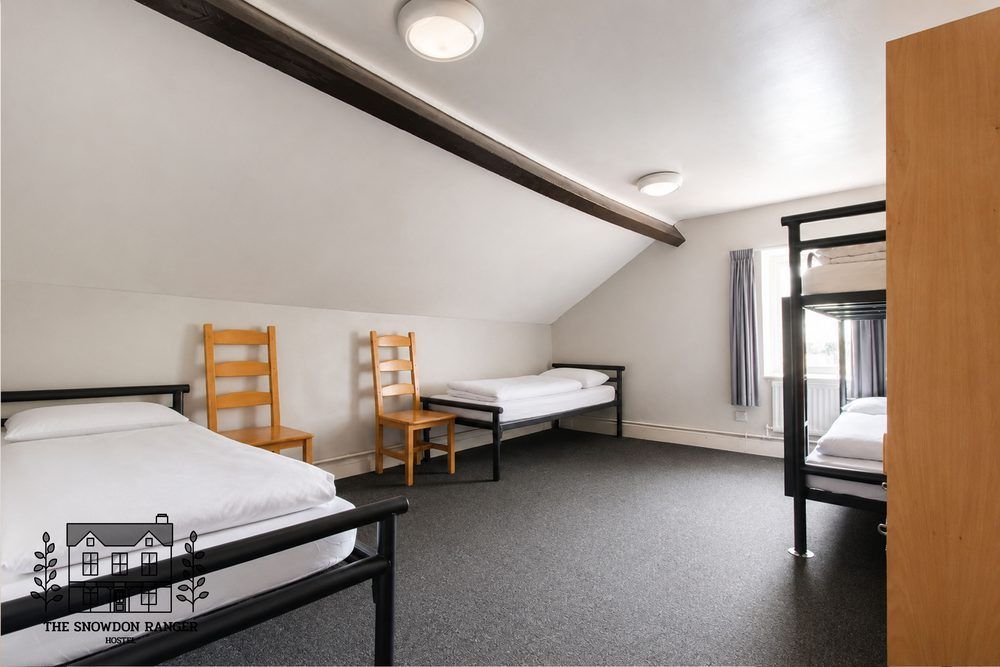 Shared attic bedroom with four single beds, white walls, sloped ceiling, and a carpeted floor