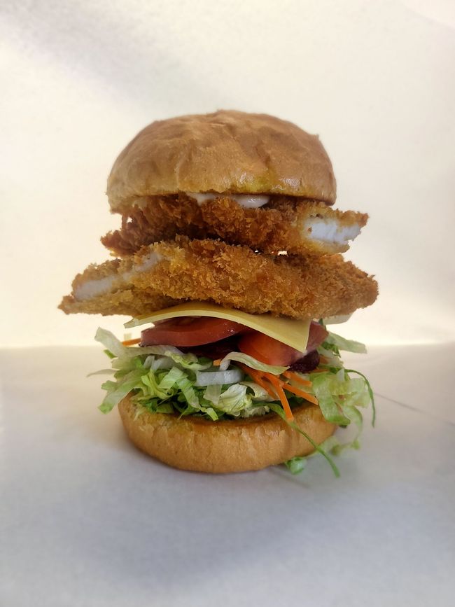 Fish sandwich with lettuce, tomato, cheese, and two fried fish pieces on a bun.