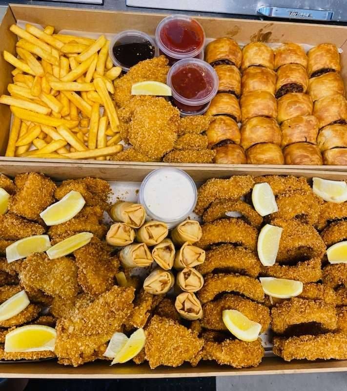 Two food trays with fried foods, sausage rolls, dips, and lemon wedges.