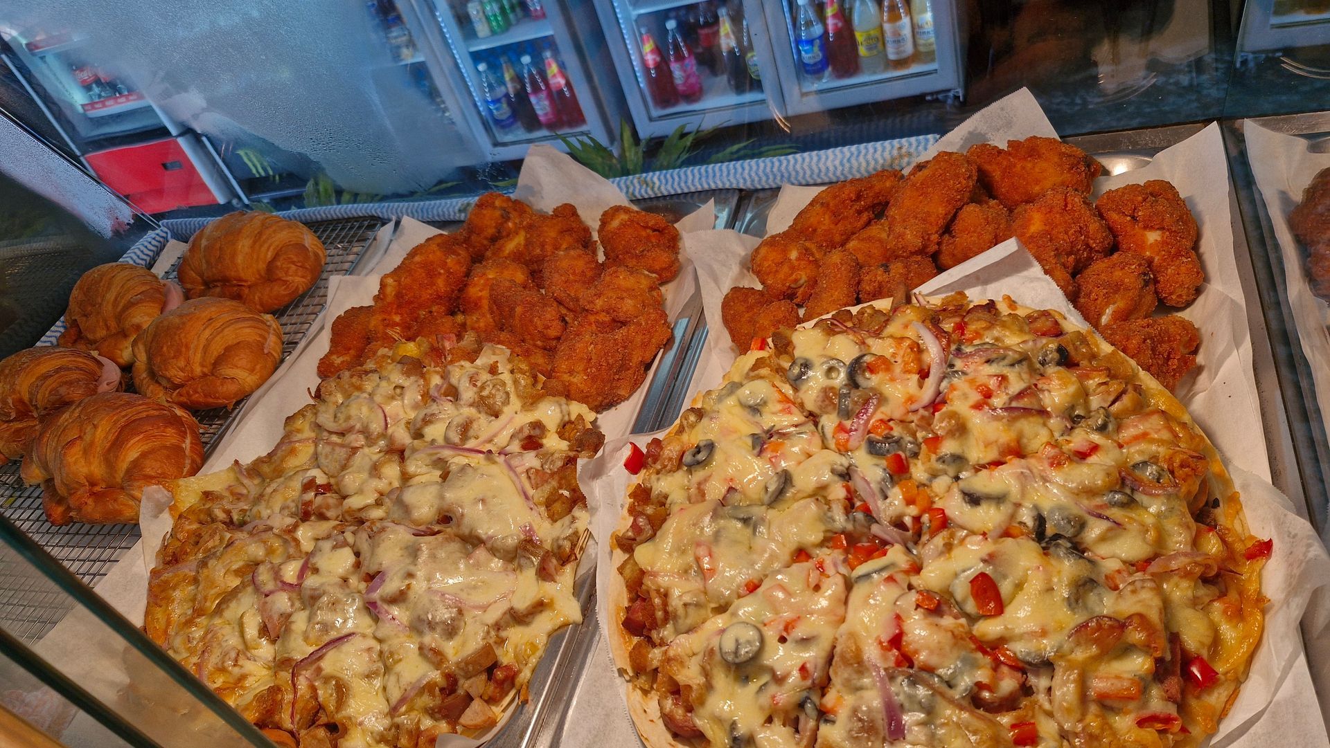 Display case of baked goods: pizzas, fried chicken, pastries. — Boundary Street Fish & Burger Bar in Railway Estate, QLD