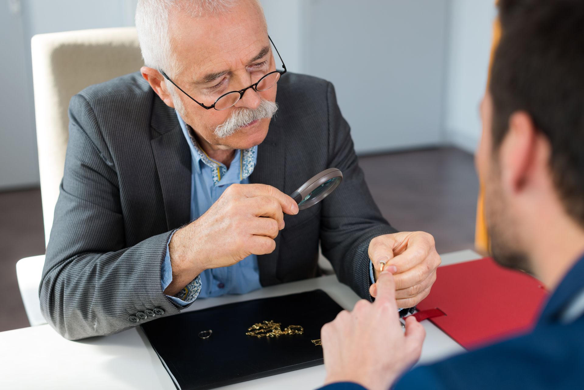 A man is looking through a magnifying glass at a piece of jewelry.