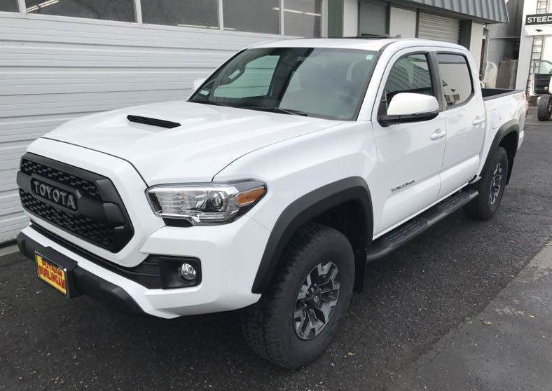 White Toyota Tacoma truck parked in front of a building with a black grille and black wheel wells.