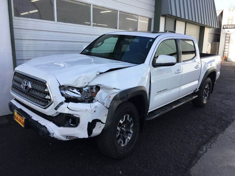 White Toyota Tacoma truck with front-end damage parked outside a building.
