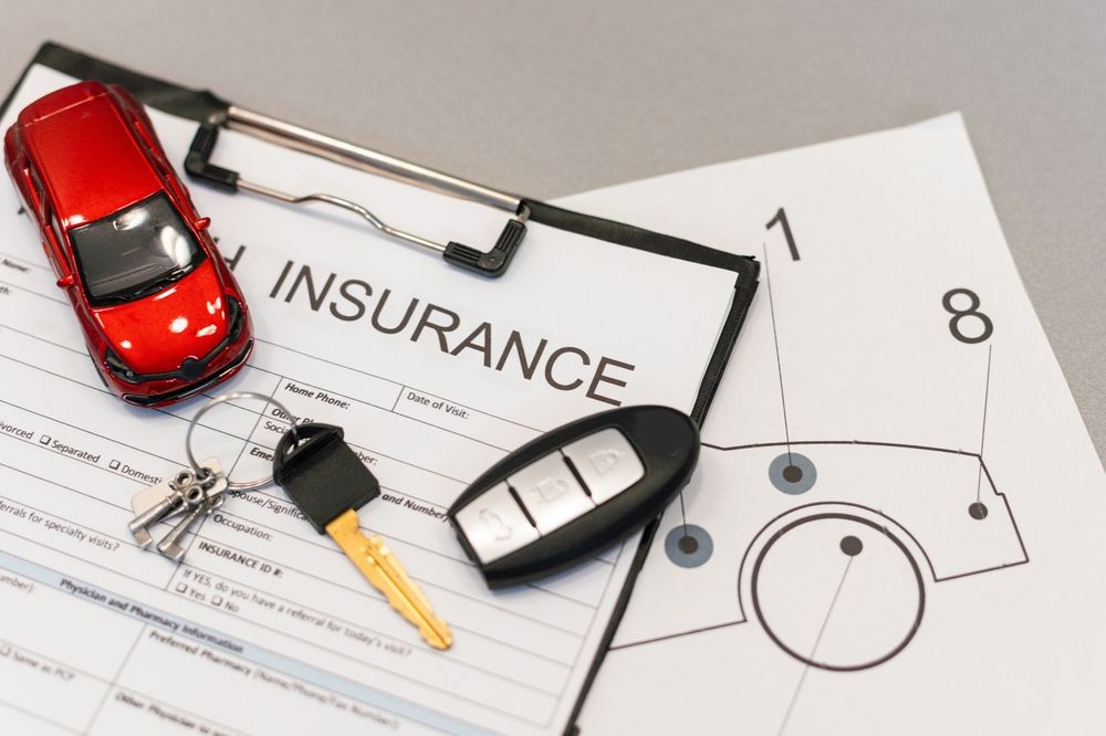 Red toy car, keys, and car remote on insurance paperwork.