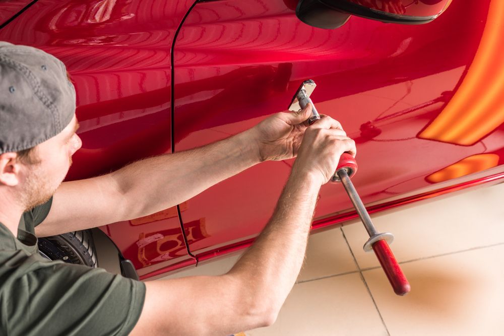 A person using a tool to repair a dent on a red car door.