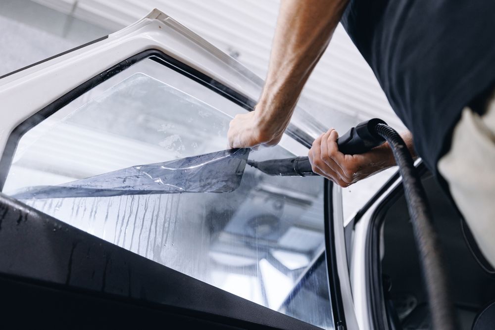 Person applying window tint to a car window with a tool, outdoors.