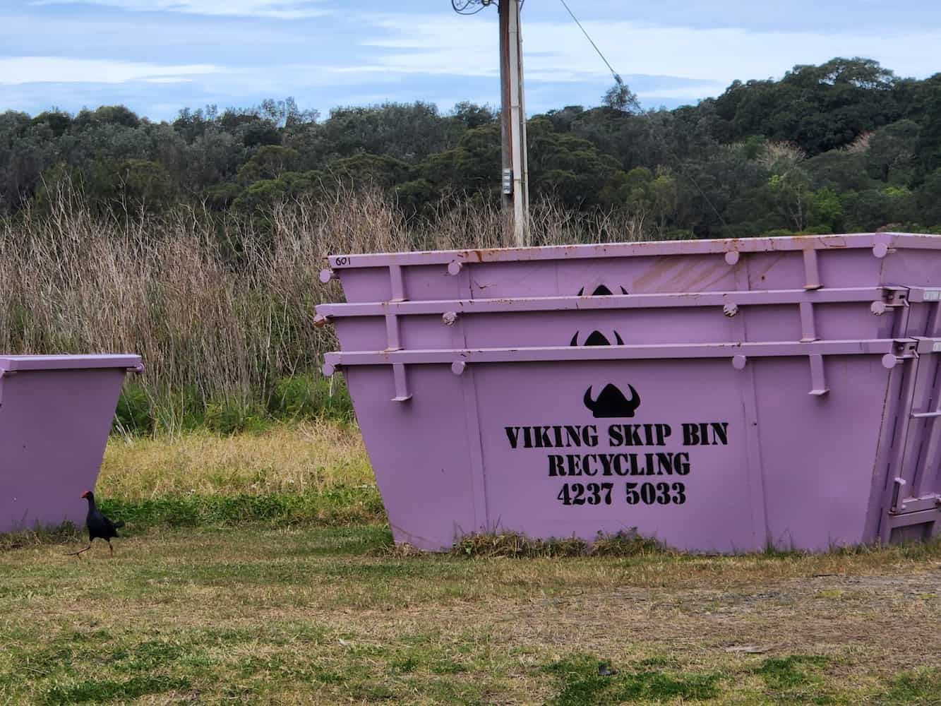 A Stack of Purple Viking Skip Bins in a Grassy Field — Viking Skip Bin Recycling In Wollongong, NSW