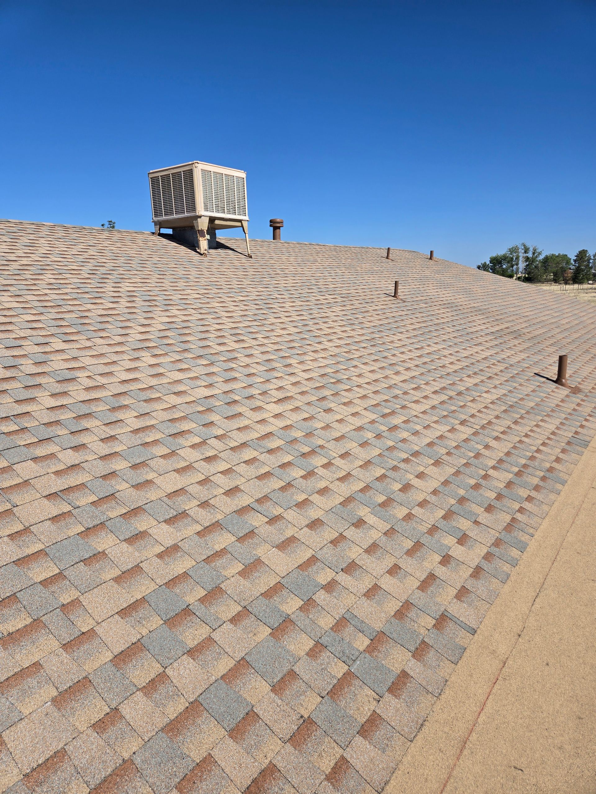 Shingled roof with a cooling unit and clear blue sky.
