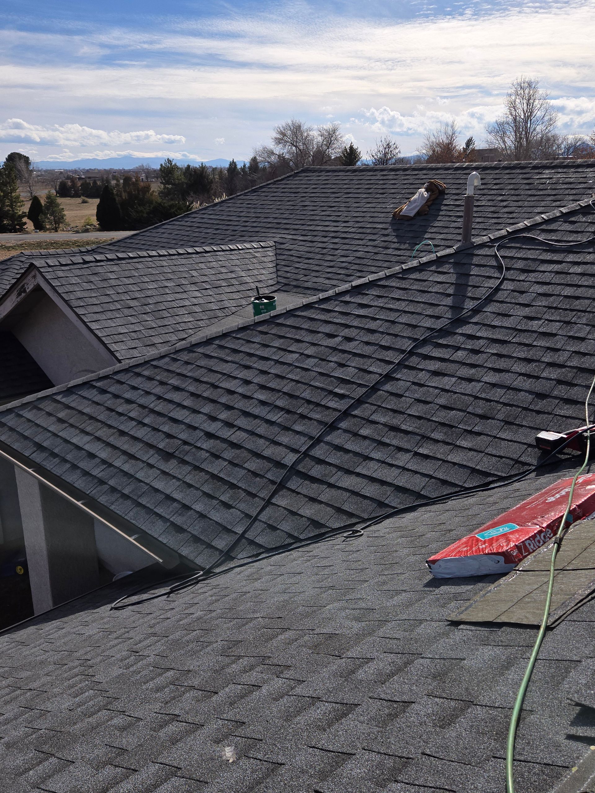 Rooftop with shingles under a partly cloudy sky, some equipment visible; a worker on the roof.