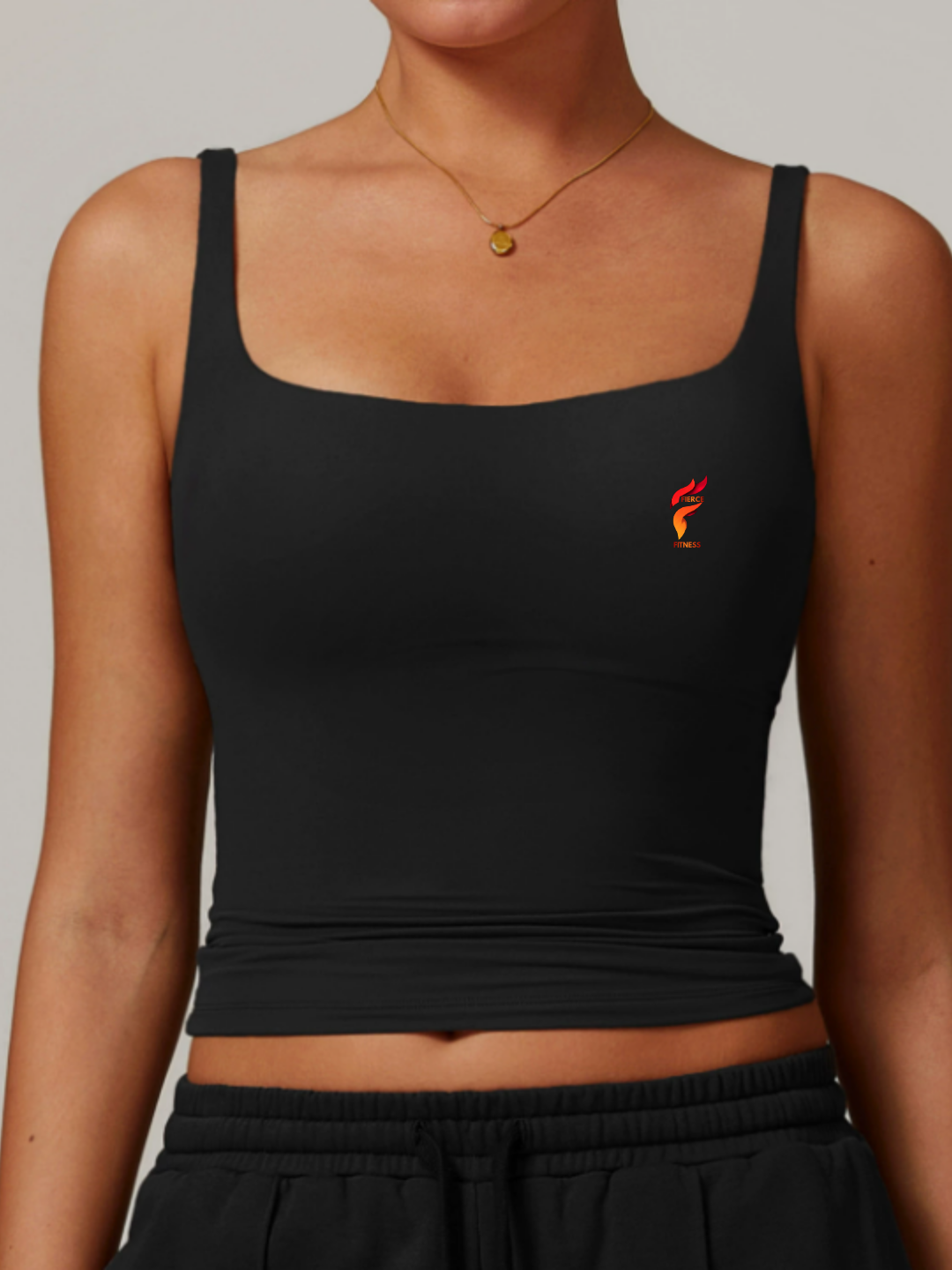 Black square-neck crop tank top with a small red-orange logo on the chest, worn with black pants