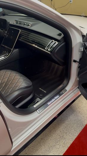 Open car door showing a black quilted interior and silver exterior trim in a garage.