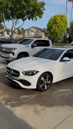 White sedan in foreground and silver pickup behind it parked on a wet suburban street