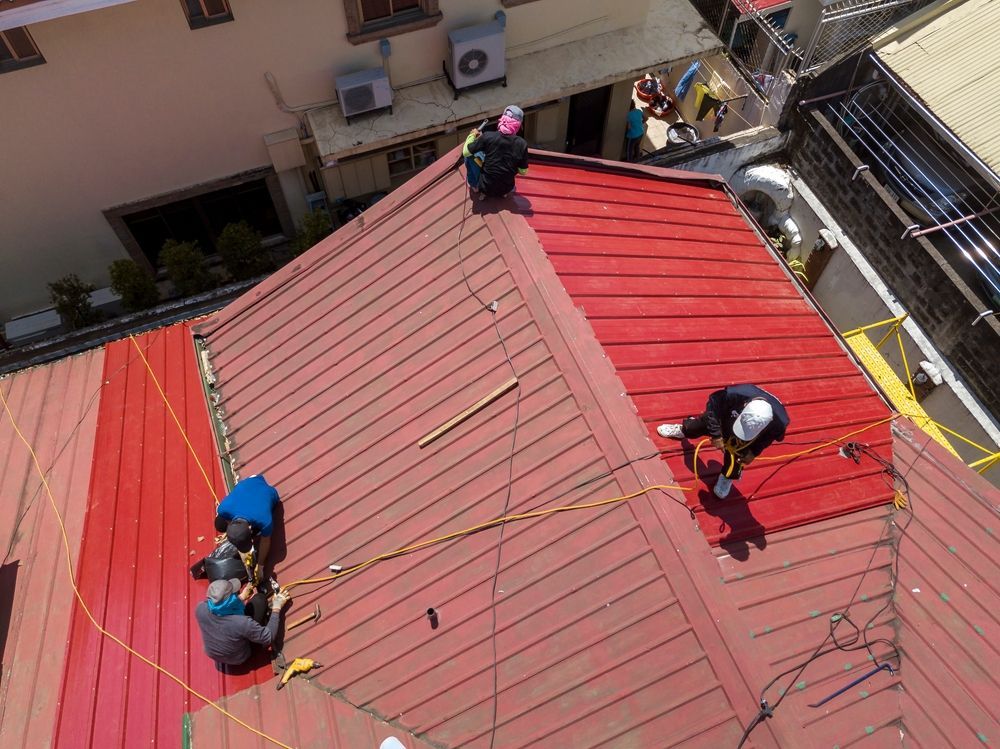 Workers in Safety Gear on a Red Metal Roof — Coral Coast Roofing in Earlville, QLD