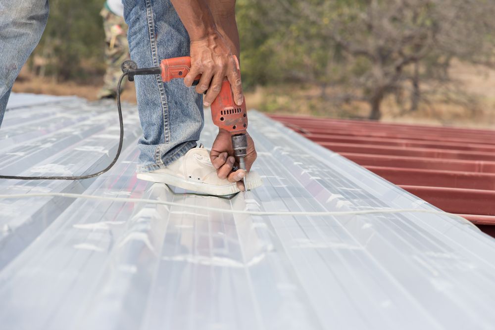 A Man is Using a Drill to Drill a Hole in a Metal Roof — Coral Coast Roofing In Mission Beach, QLD