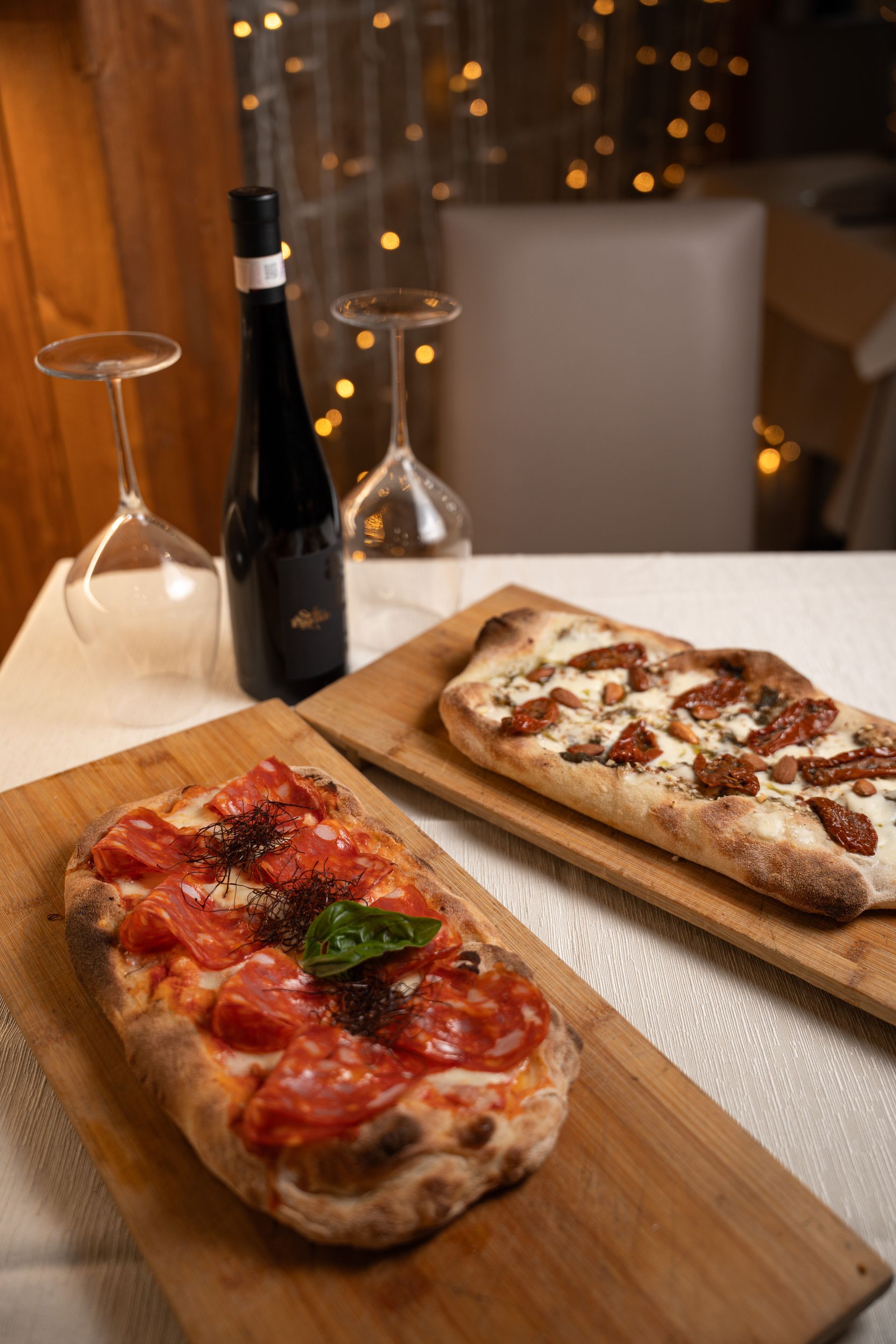 Due pizze rettangolari su assi di legno, con una bottiglia di vino e dei bicchieri.