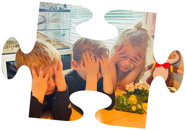 Een jong kind in een roze jasje zit in een rood wagentje, getrokken door een jongen op een gele speelgoedtractor.