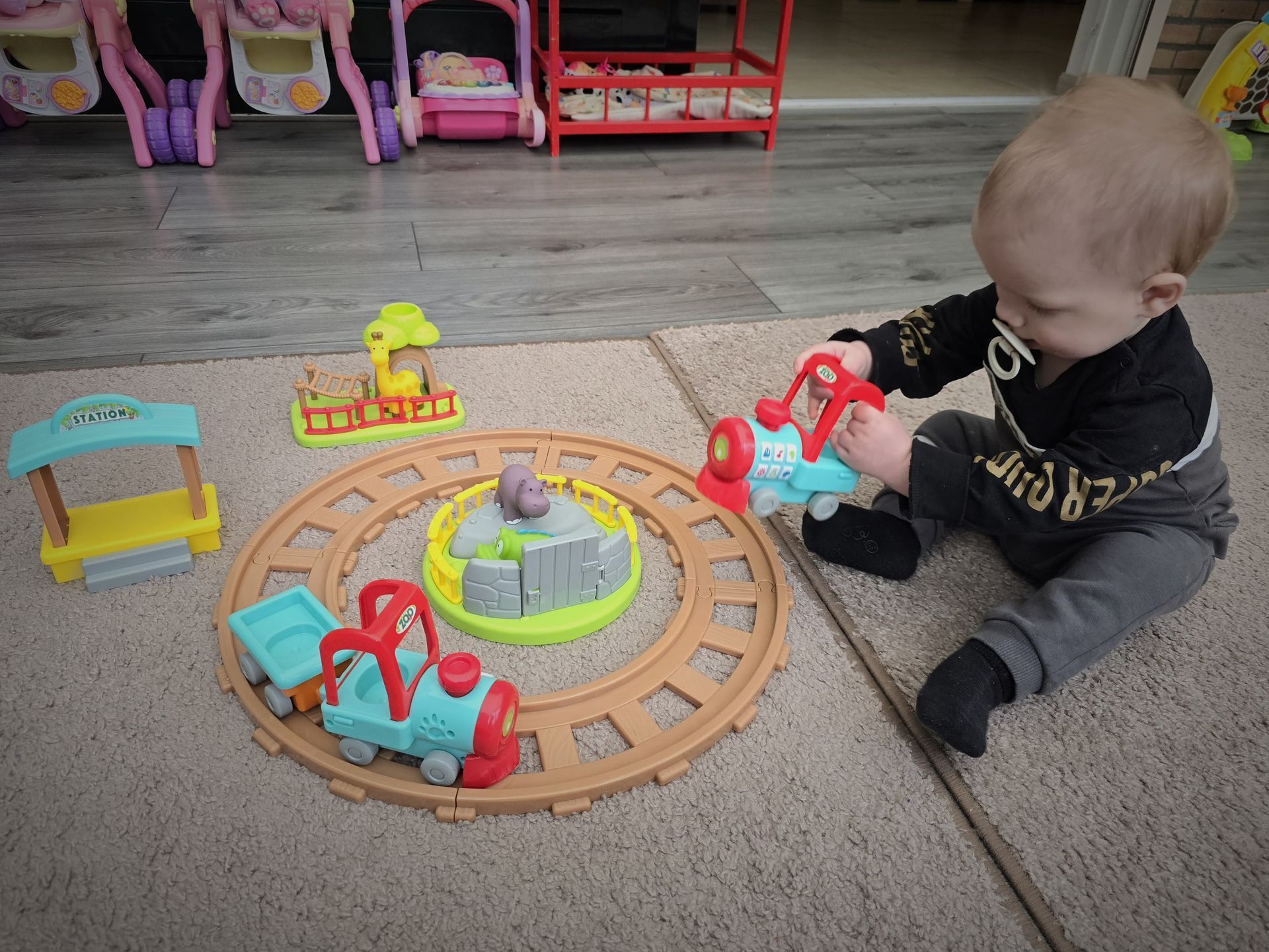 Een vrouw wijst naar twee kinderen die tegen een houten hek leunen, naast een kinderwagen.