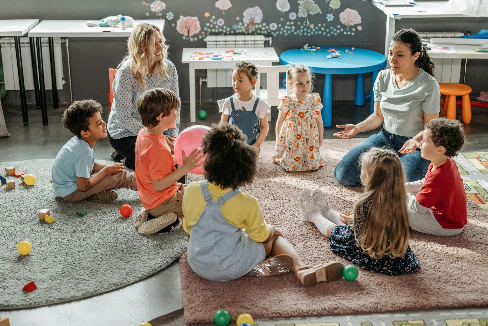 Twee leerkrachten leiden een groep kinderen in een kring op een kleed. Klaslokaalopstelling.