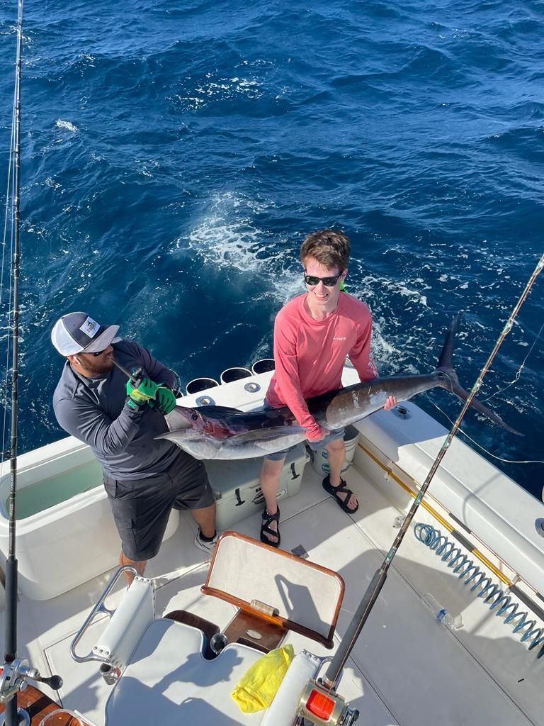 two men are holding a large fish on a boat in the ocean .