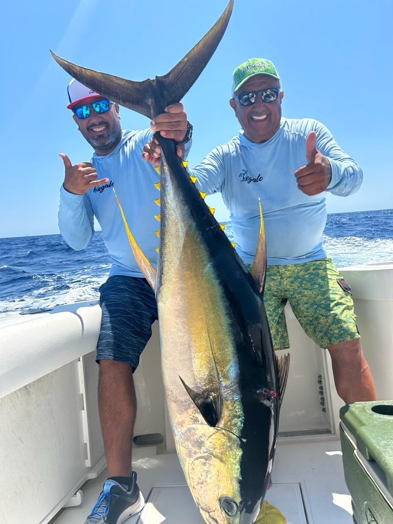 two men are holding a large fish on a boat and giving a thumbs up .