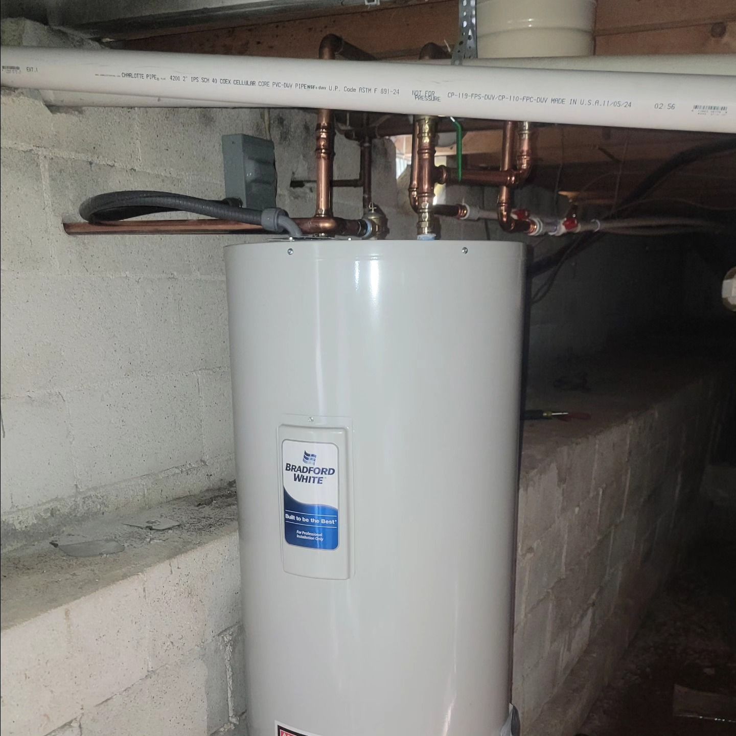 A white water heater in a basement with copper pipes