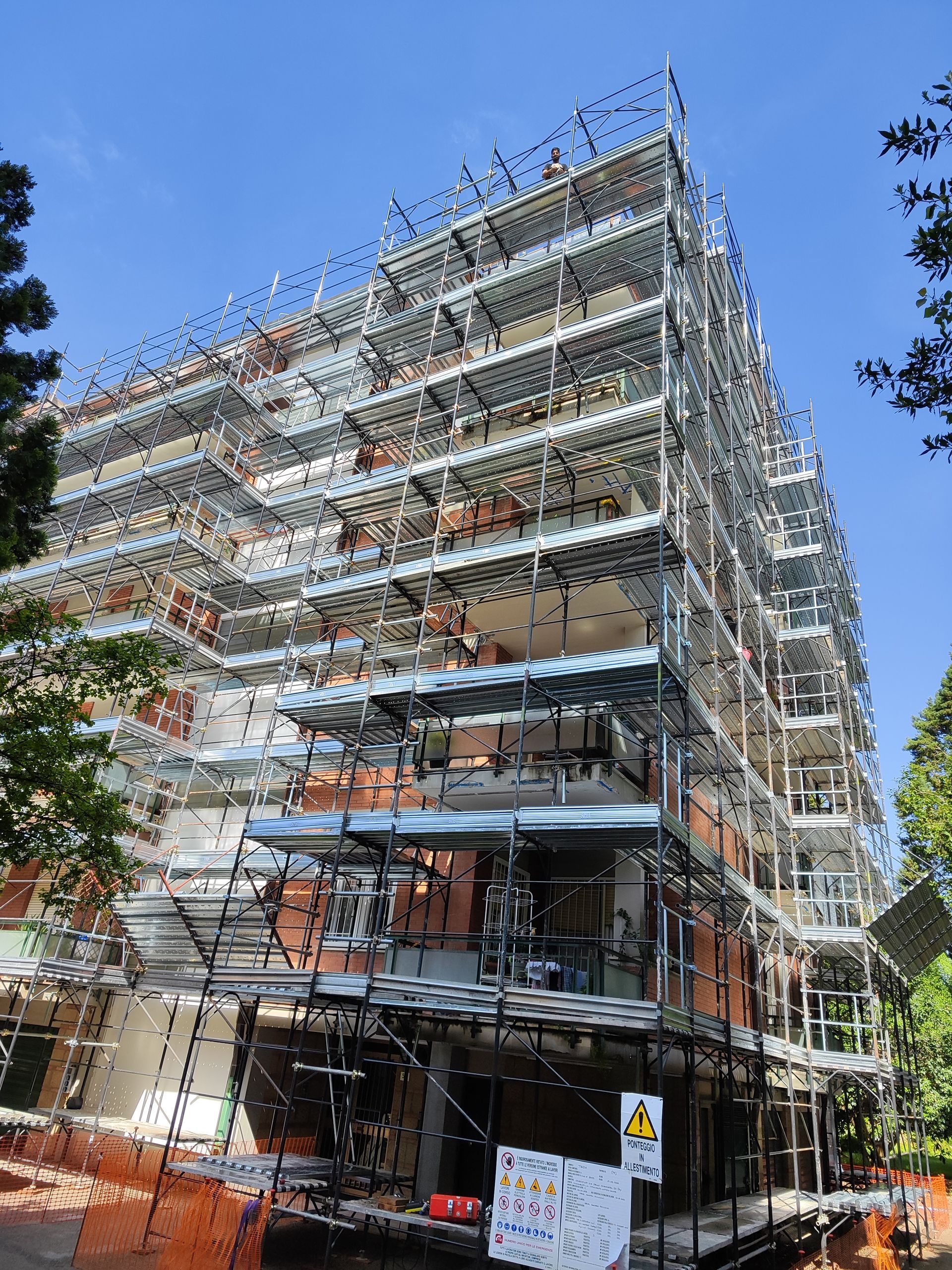 Edificio in costruzione, un'impalcatura copre la facciata, rete di sicurezza arancione.