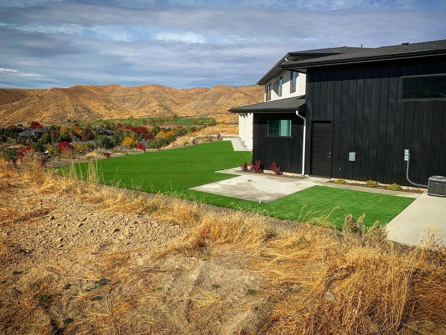 Black-sided house with green lawn overlooking arid hills and a partly cloudy sky.
