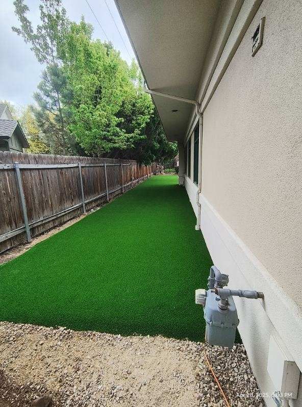Long strip of green artificial turf next to a building and wooden fence.