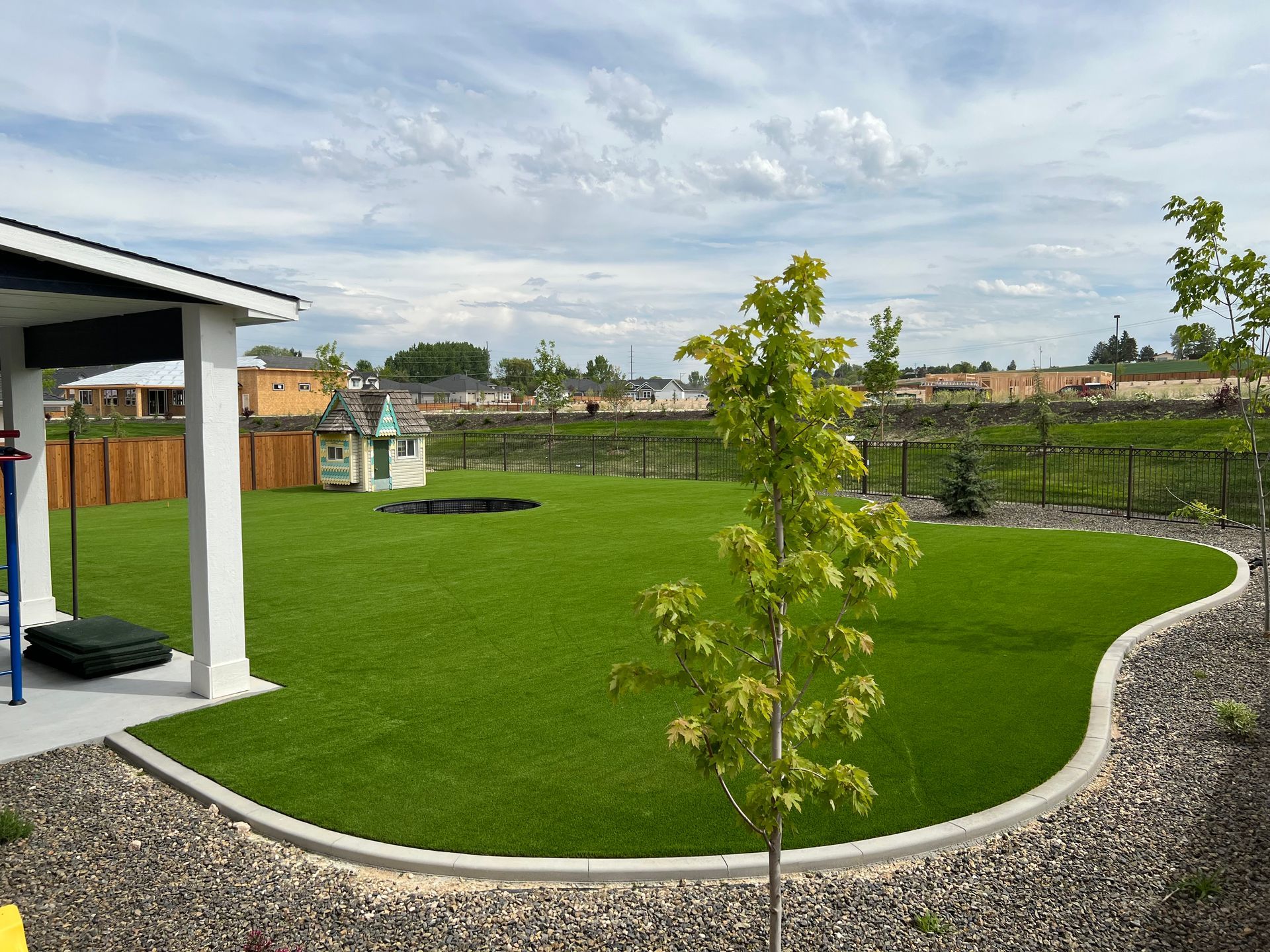 A well-manicured lawn with a small tree and playhouse. Stone border curves around the grass.