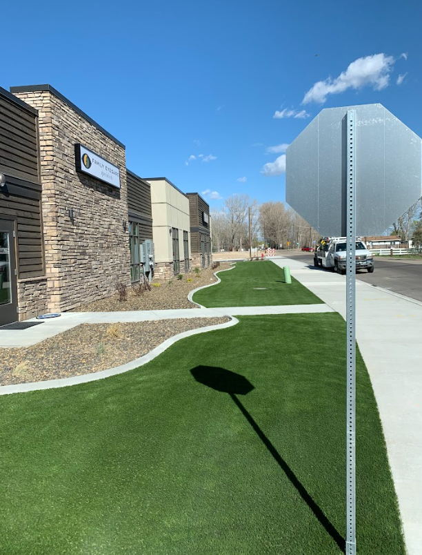 Building with a sign, lush green lawn, sidewalk, stop sign, sunny day.