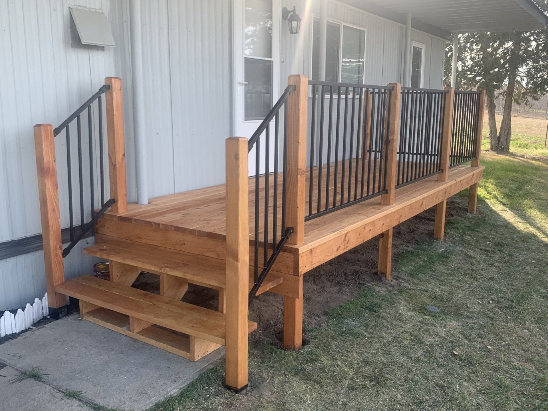 Wooden deck with black railings and steps leading to a house entrance on a grassy lawn.