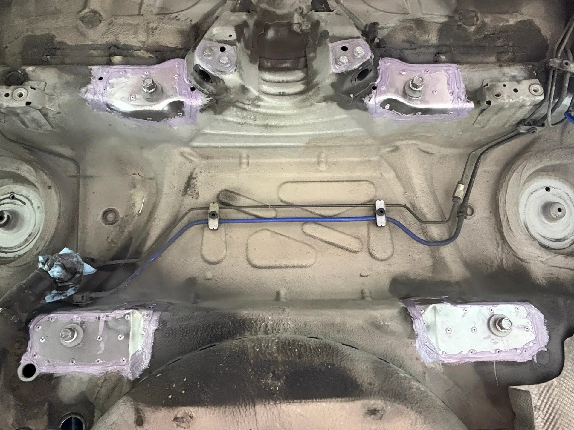 Undercarriage of a vehicle with four visible mounting points coated in pinkish-purple material. Fuel lines and other components are also visible. | GermanTech MotorWorks, LLC