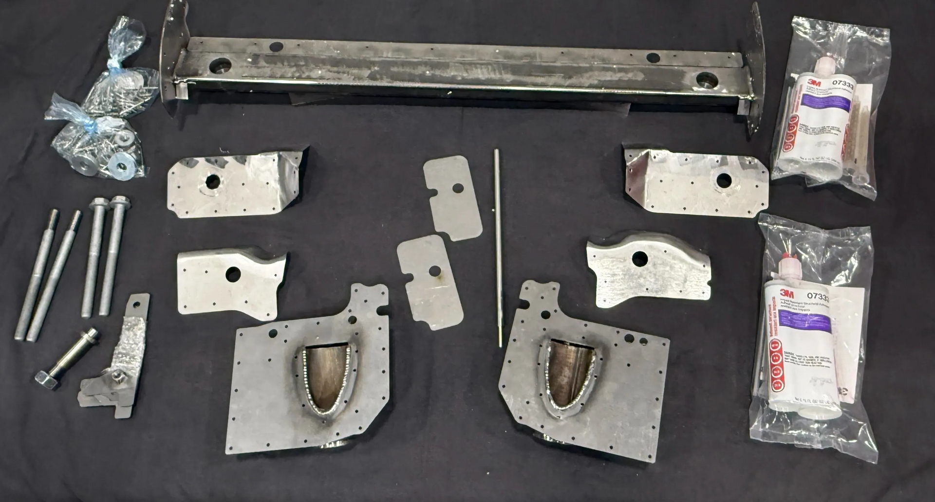 Metal car parts laid out on a black surface; bolts, brackets, and a bumper are visible. | GermanTech MotorWorks, LLC