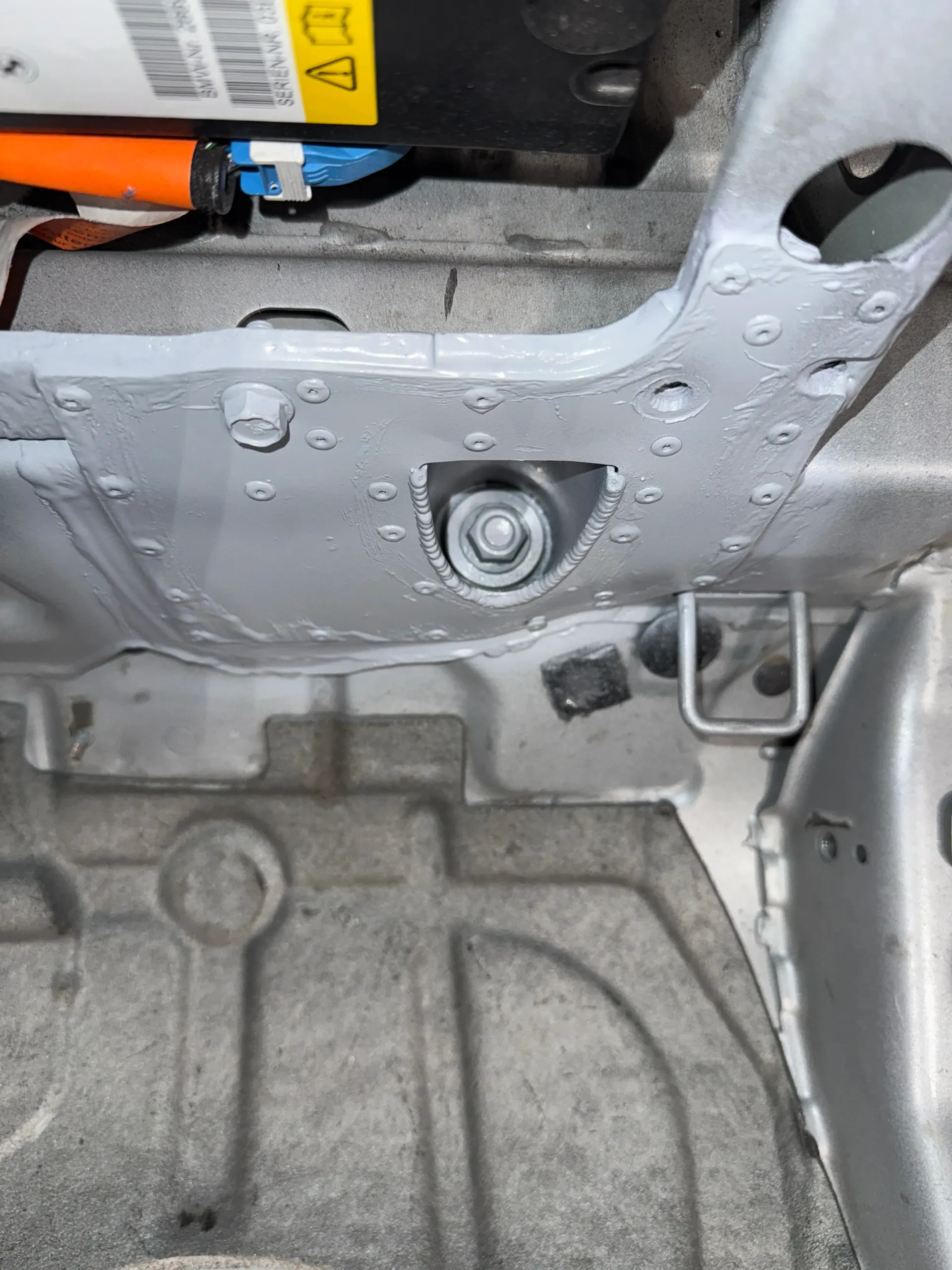 Undercarriage of a vehicle, showing a silver-painted metal structure with a bolt, electrical components visible in the background. | GermanTech MotorWorks, LLC