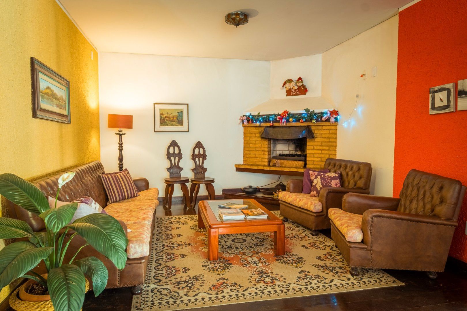 Sala de estar aconchegante com sofá verde, poltronas marrons, mesa de centro, lareira e paredes amarelo-alaranjadas.
