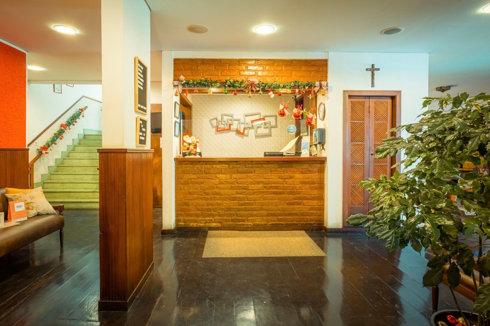 Hall de entrada com balcão de recepção, painéis de madeira, piso escuro brilhante e planta em vaso.