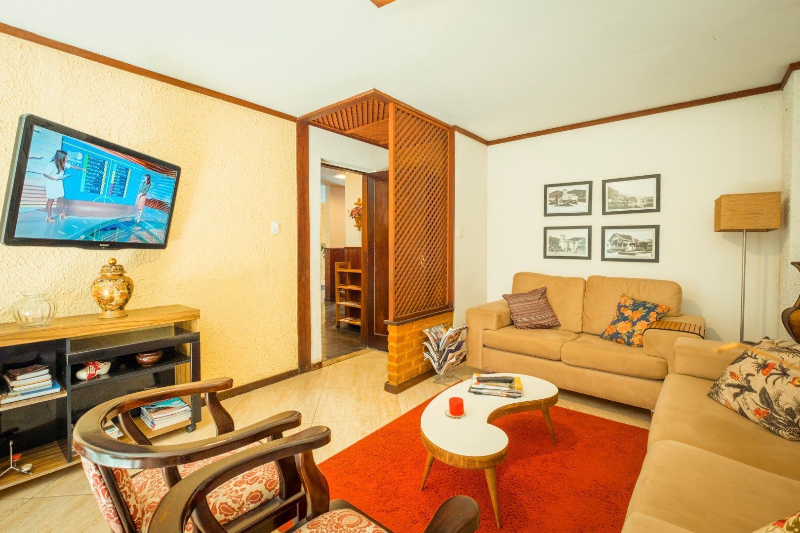 Sala de estar aconchegante com sofás bege, tapete vermelho, mesa de centro, TV de parede e detalhes em madeira em tons quentes.