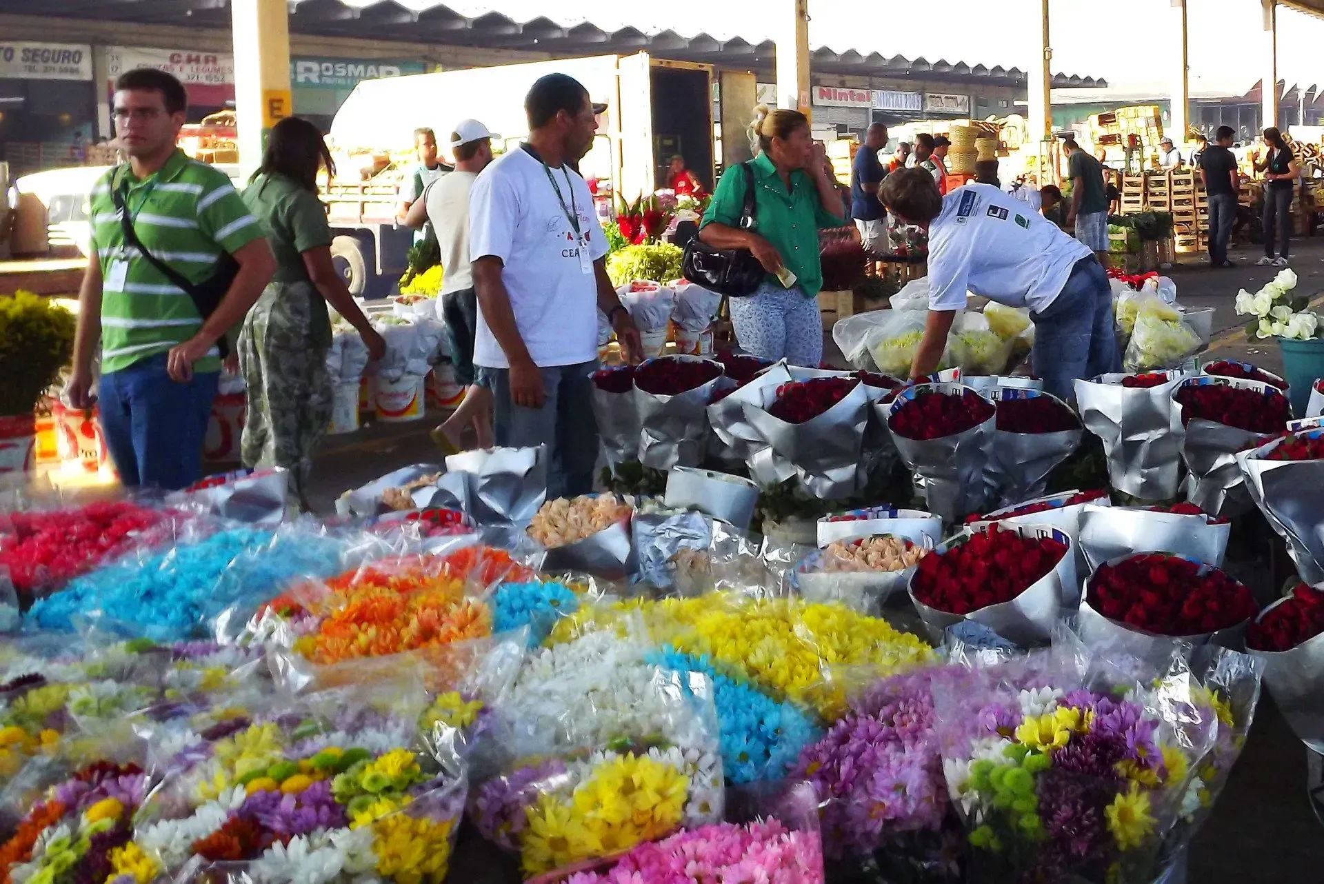 Bancas de mercado de flores com baldes de buquês coloridos e vendedores olhando as flores ao ar livre.
