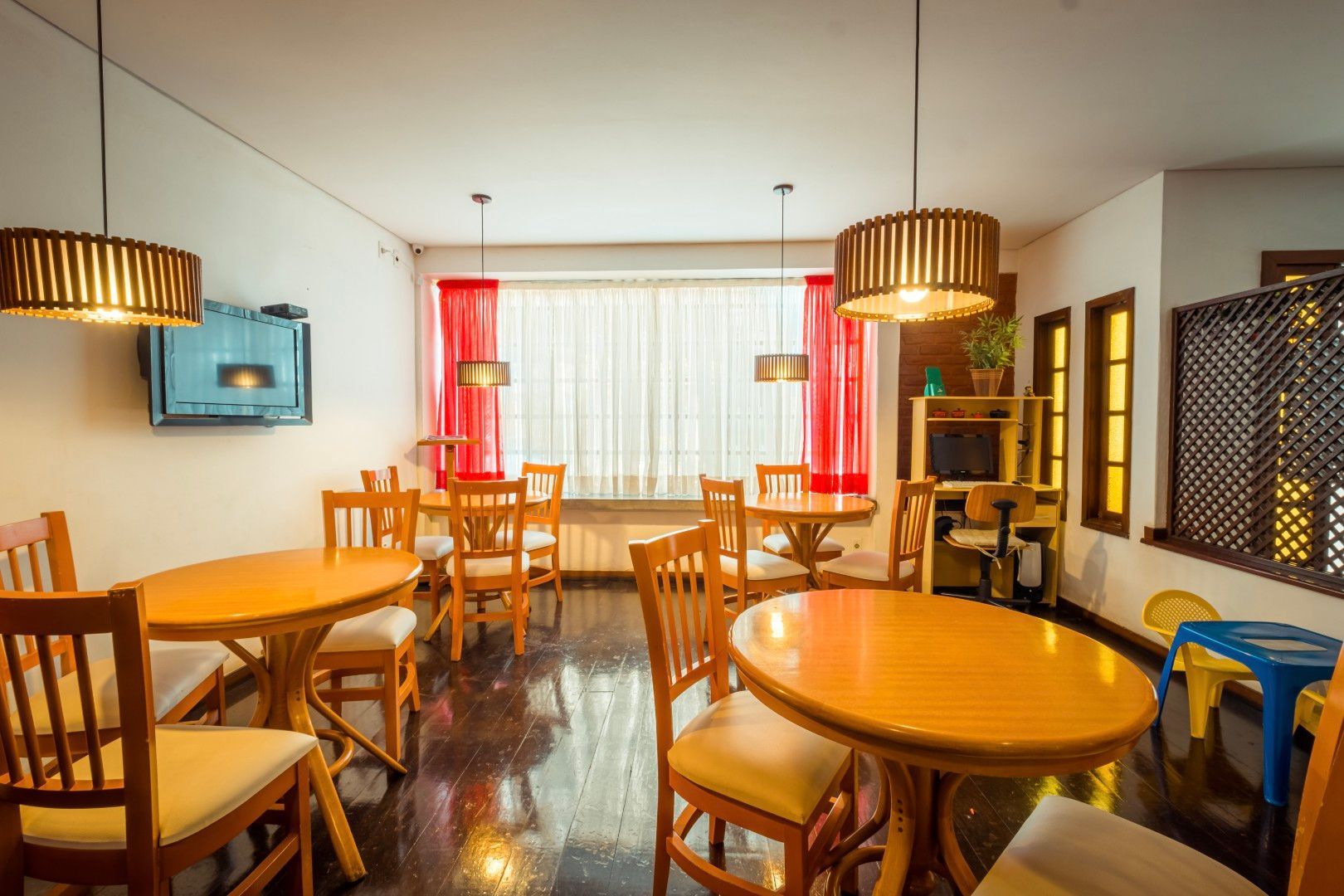 Interior aconchegante de um café com mesas e cadeiras de madeira, luminárias pendentes e cortinas vermelhas na janela.