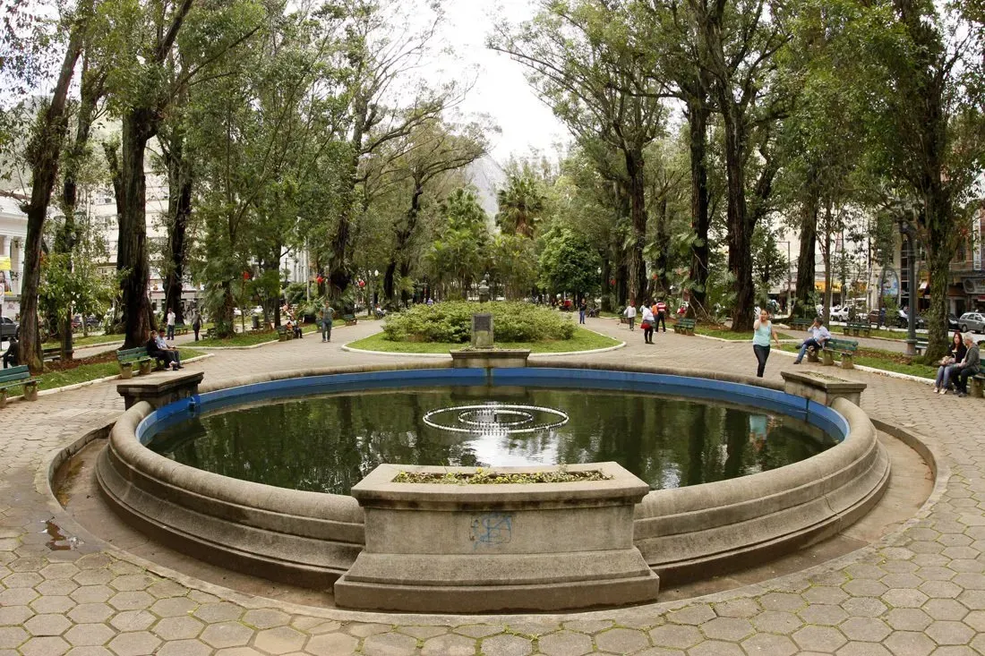 Fonte circular em um parque arborizado com bancos e caminho pavimentado.