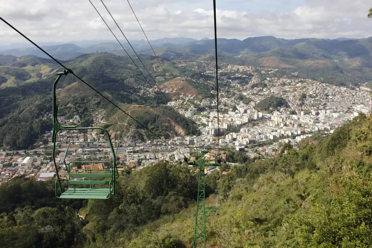 Teleférico sobre colinas verdejantes com uma cidade que se estende por um vale montanhoso.