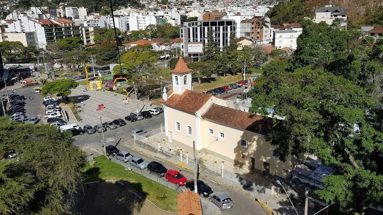 Vista aérea de uma igreja histórica com telhados de telha vermelha ao lado de uma estrada e carros estacionados em um bairro da cidade.
