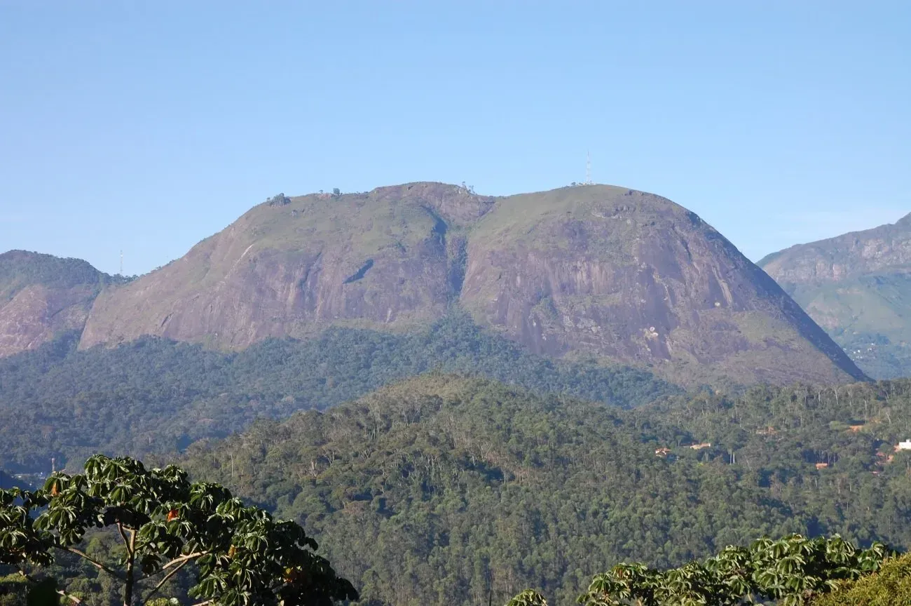 Cordilheira sob um céu azul límpido, com encostas verdejantes e arborizadas em primeiro plano.