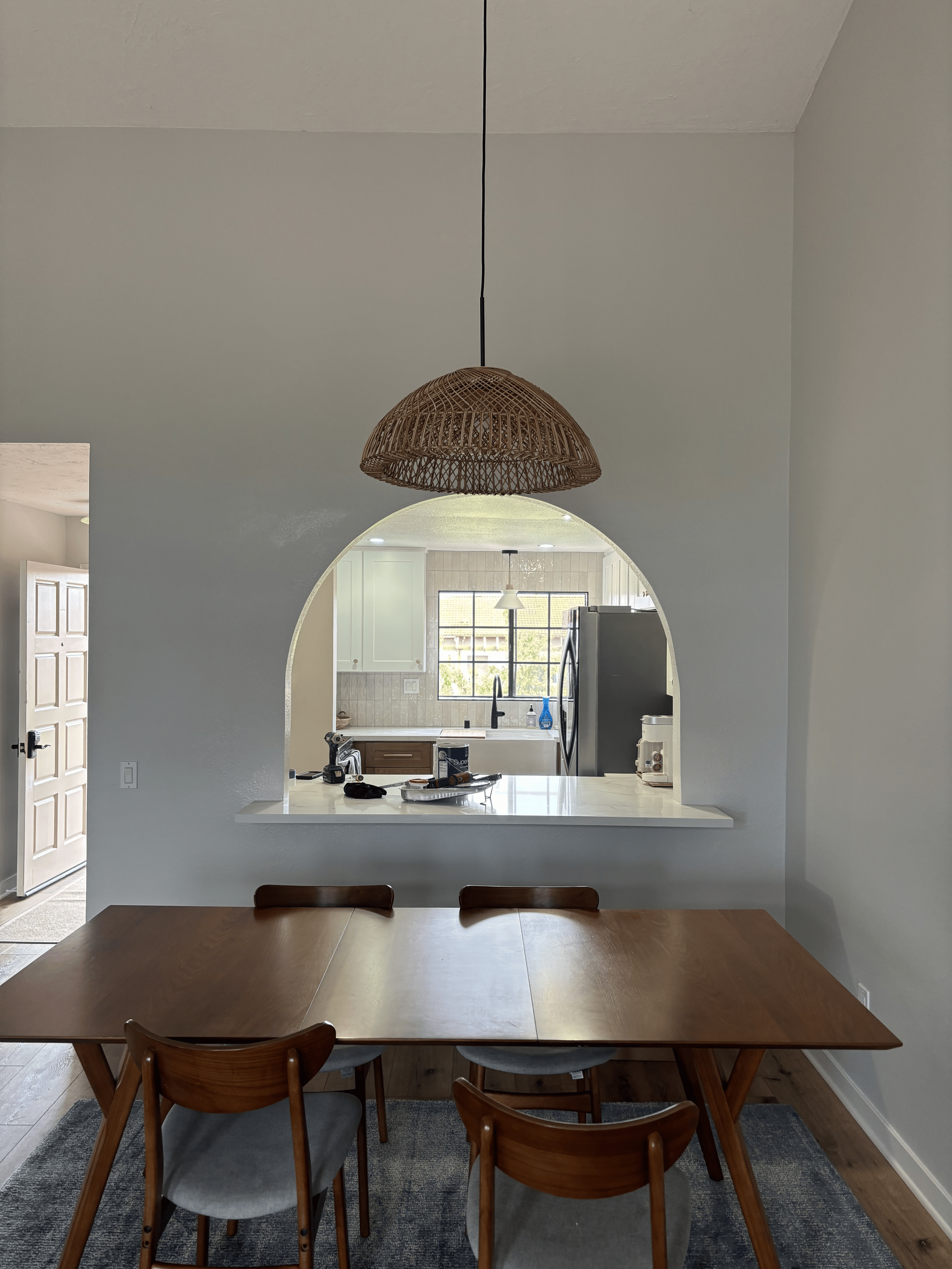 A dining room with a table and chairs and a kitchen in the background.