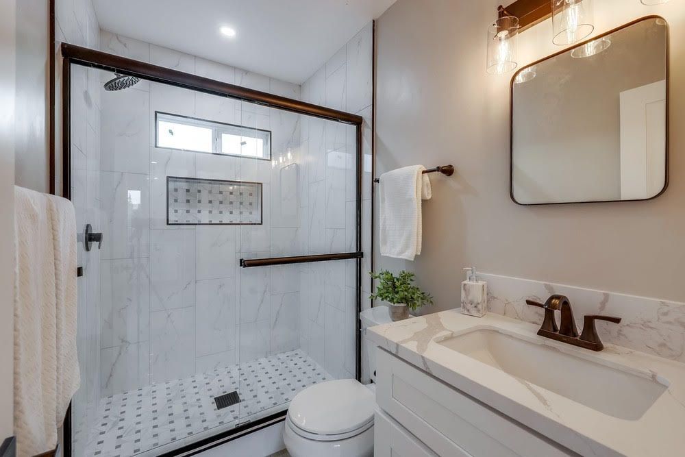 A bathroom with a toilet , sink , shower and mirror.
